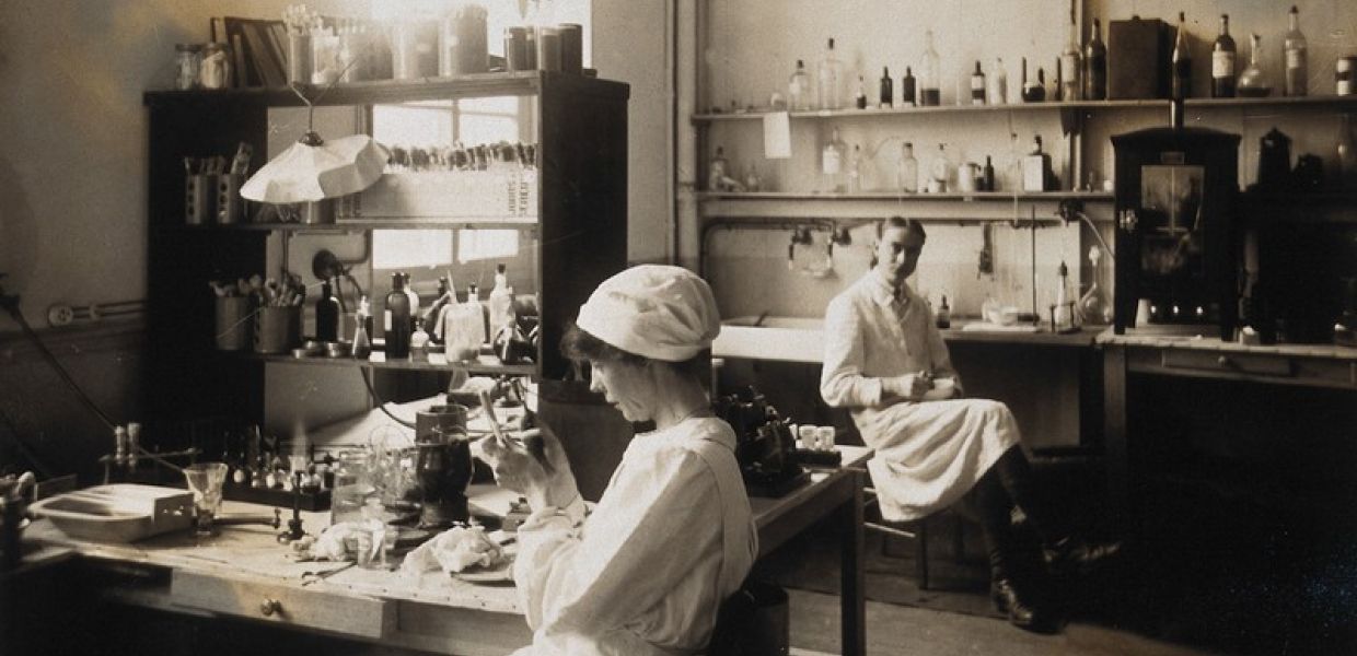 A nurse sat in a laboratory examining a small object with a magnifying glass