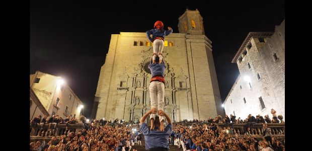 People standing on each others shoulders in front of a crowd and a cathedral
