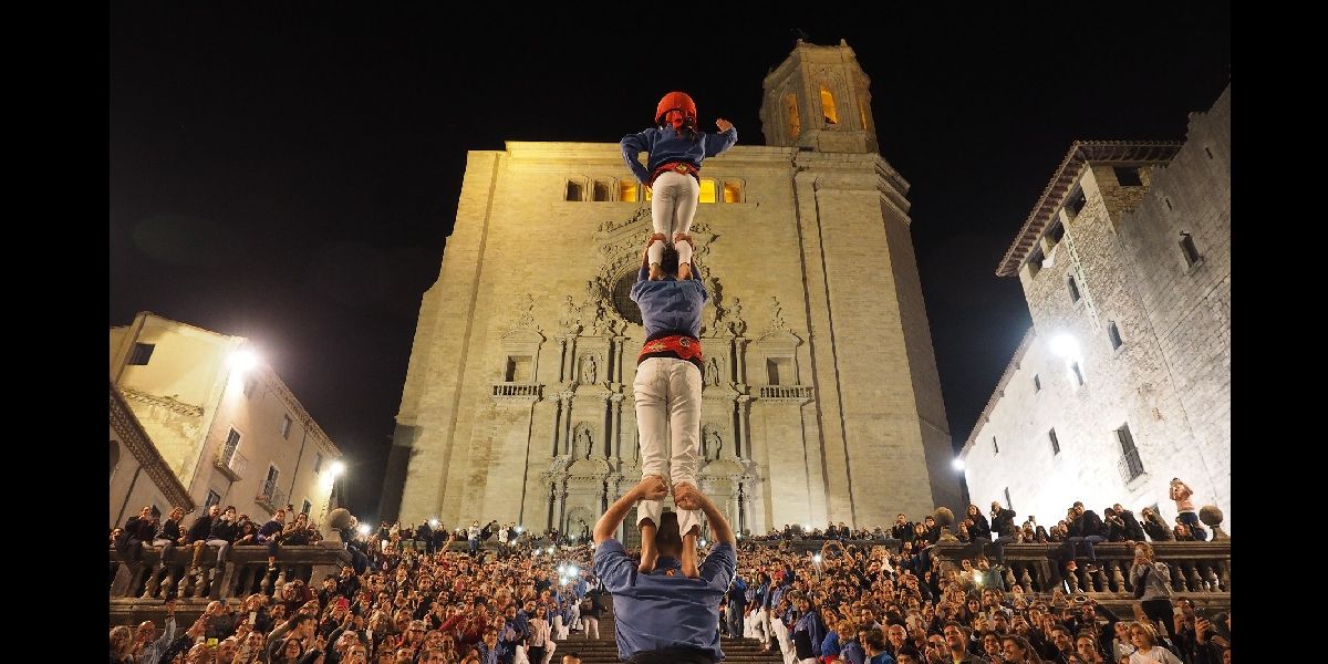 People standing on each others shoulders in front of a crowd and a cathedral