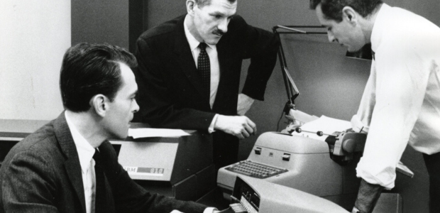 Three people looking at a typewriter
