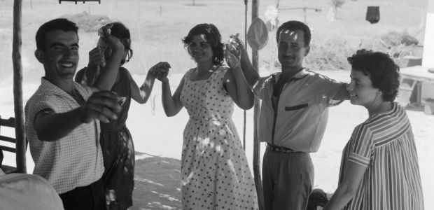 Five people dressed in summer clothes, holding hands and dancing