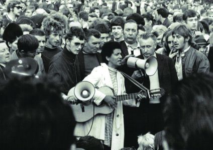 A photograph of Fasia Johnson signing and playing guitar in a crowd