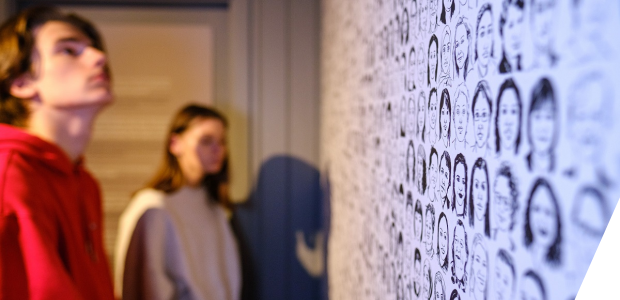 Museum visitors looking at a wall with sketches of women's faces on it