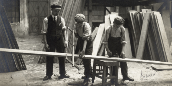 Three men working to saw a long piece of wood