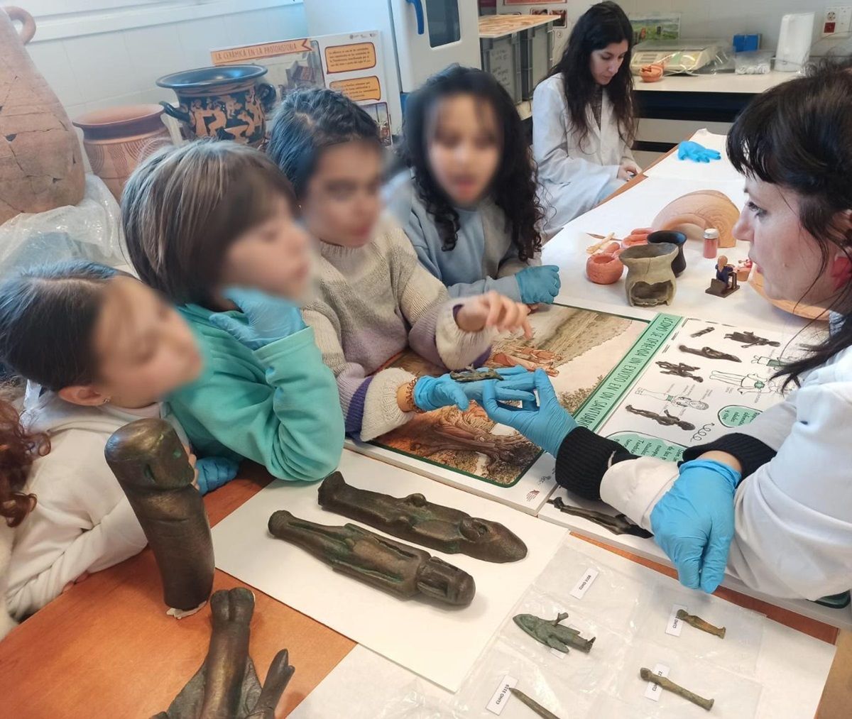 A woman holds out an artefact which two children are looking at