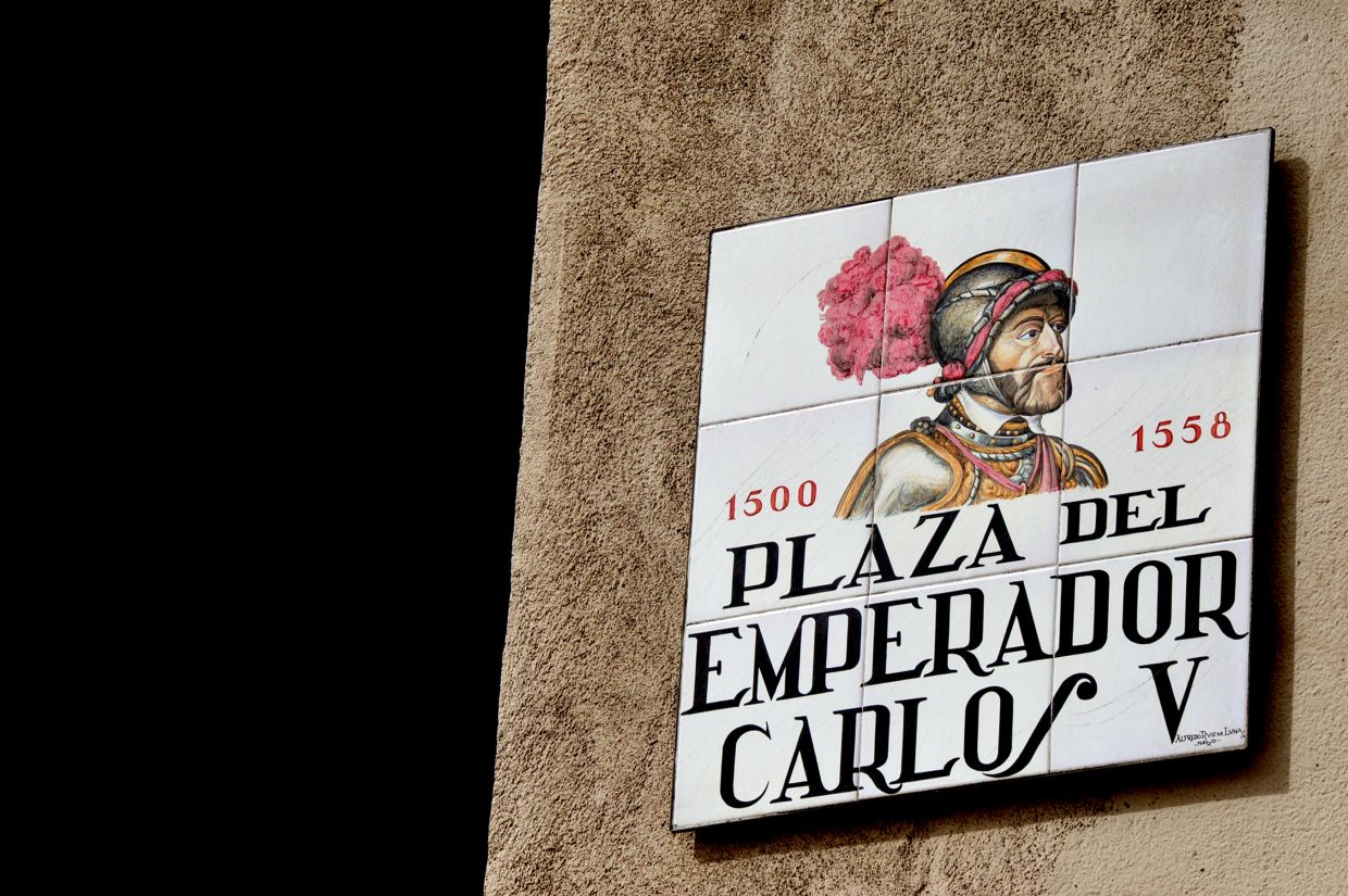A tile road sign for Plaza del Emperador Carlos V, 1500 - 1558, and an illustration of a man in a knights helmet. ©ChameleonsEye / Shutterstock
