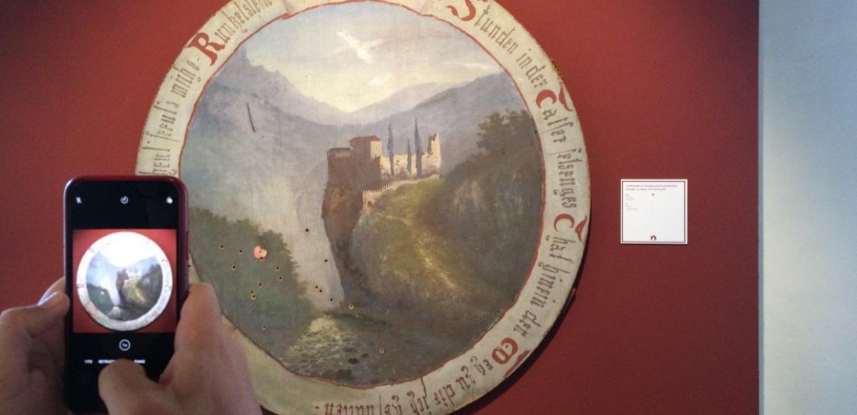 A smartphone held up to and capturing a round painting of a castle