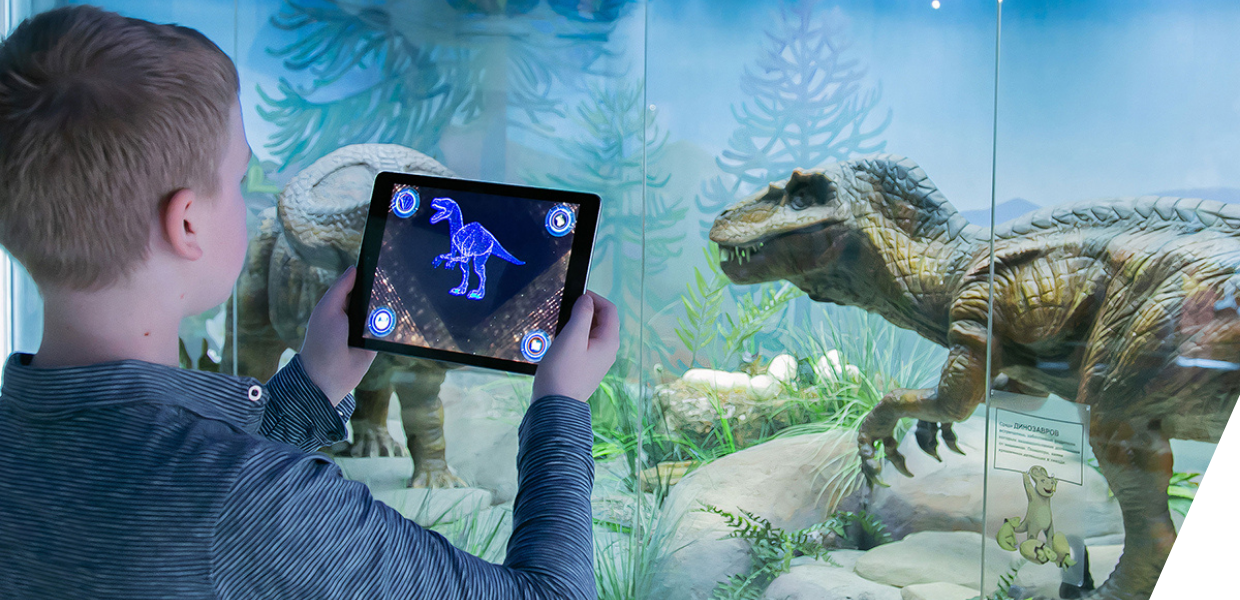 Child holding up a tablet device in front of an exhibit of a dinosaur