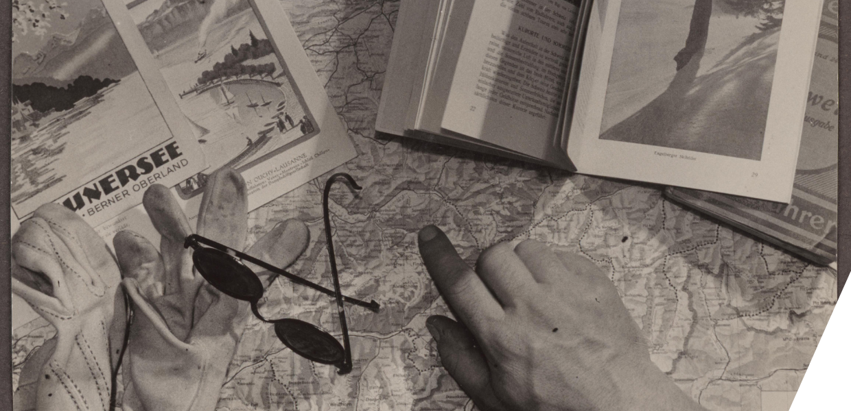 Seen from above, hands pointing at a map, on which books and sunglasses also lie on