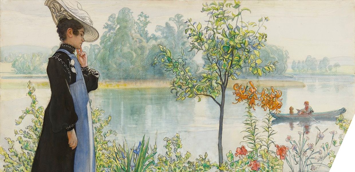 A woman in a long dress and hat stands beside a lake, looking at the colourful flowers which grow next to it