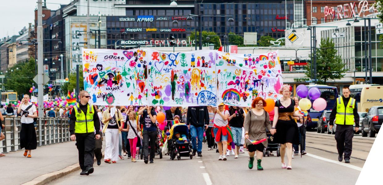 A group of people walk down a road carrying a colourful painted banner and balloons
