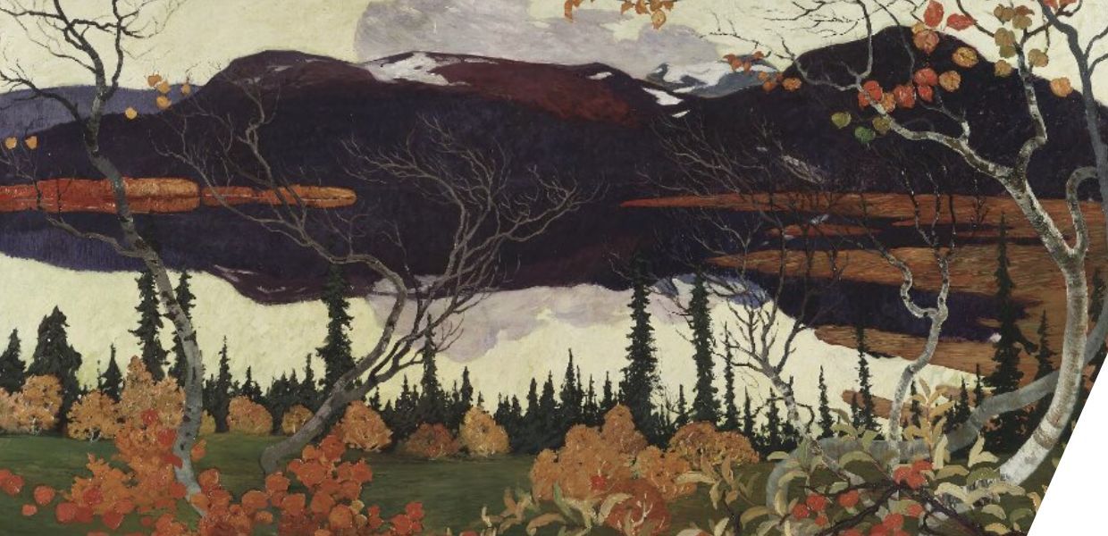 An autumn scene showing branches with orange and yellow leaves in the foreground. In the background are trees, a lake and mountains.