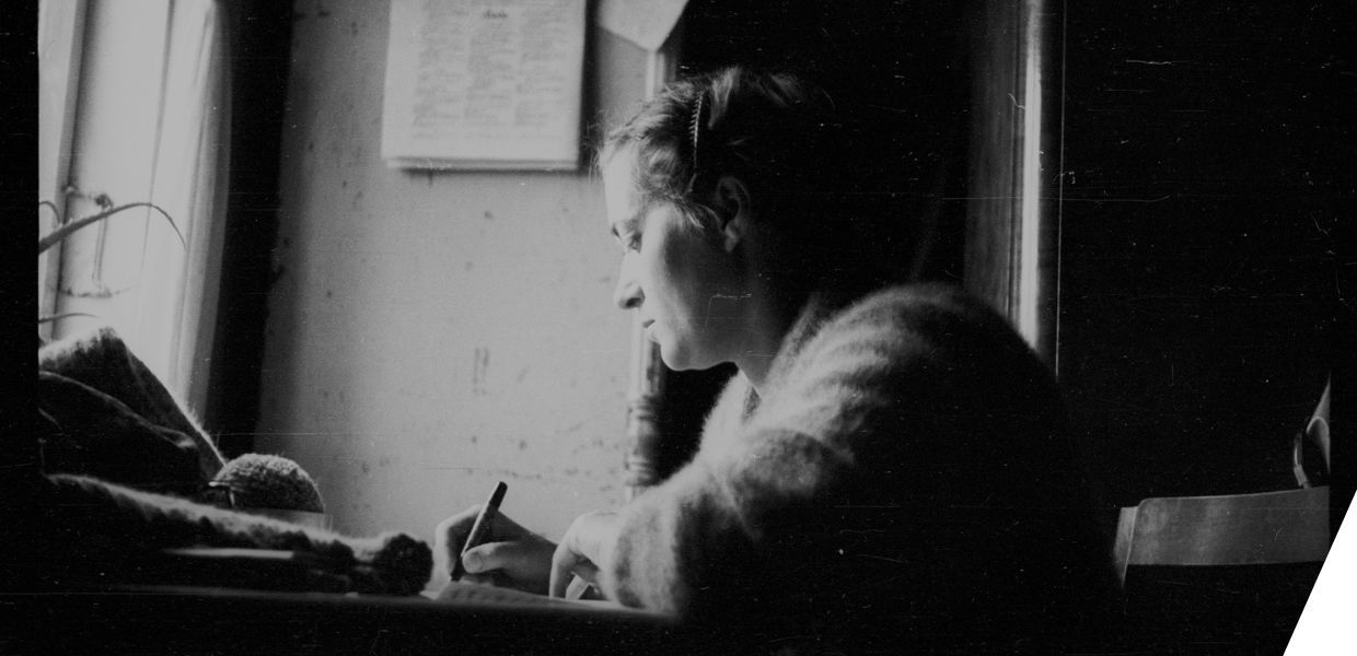 A black and white photograph of a woman writing at a desk