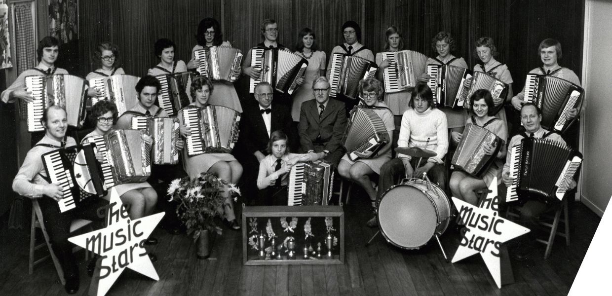 A photograph of a band of accordion players. Two plastic stars at the front indicate the band name, the music stars. 