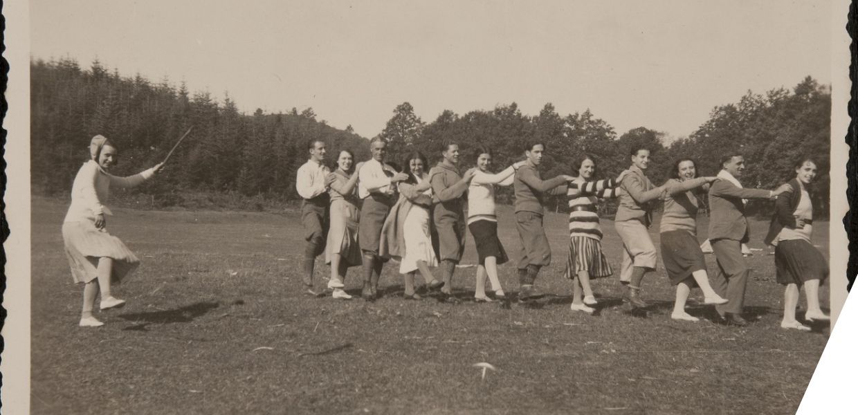 Young men and women dance together while a girl conducts the group holding a stick