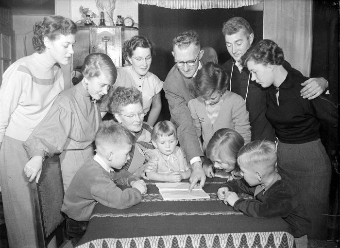 family with 10 children standing around a table looking at a map